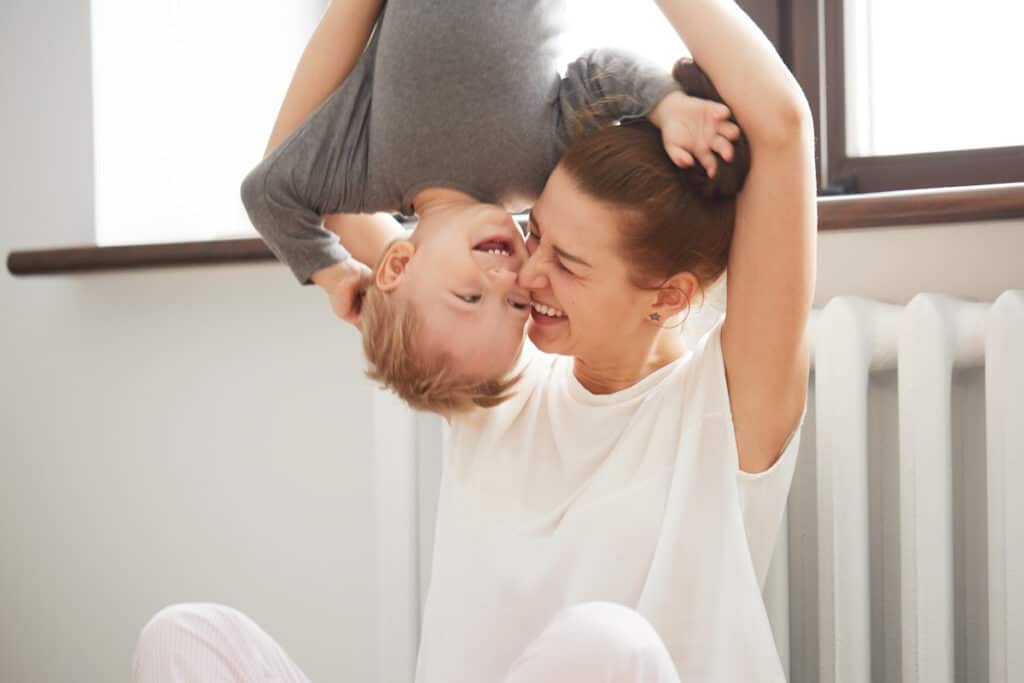 Mom laughing while holding little boy upside down.