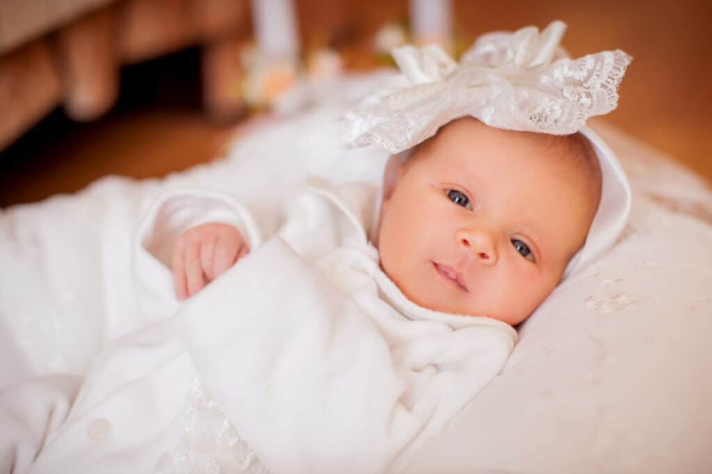 Content newborn girl in a soft outfit on a white blanket.