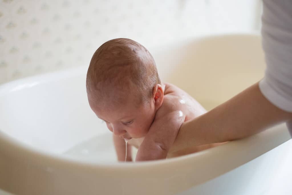 Mom bathing newborn in a bathtub.