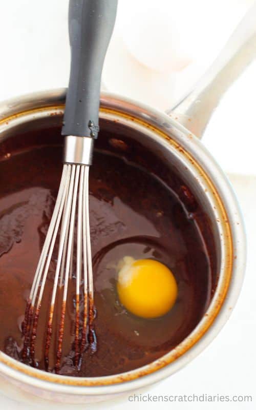 Whisking eggs into melted chocolate mixture in a metal saucepan.