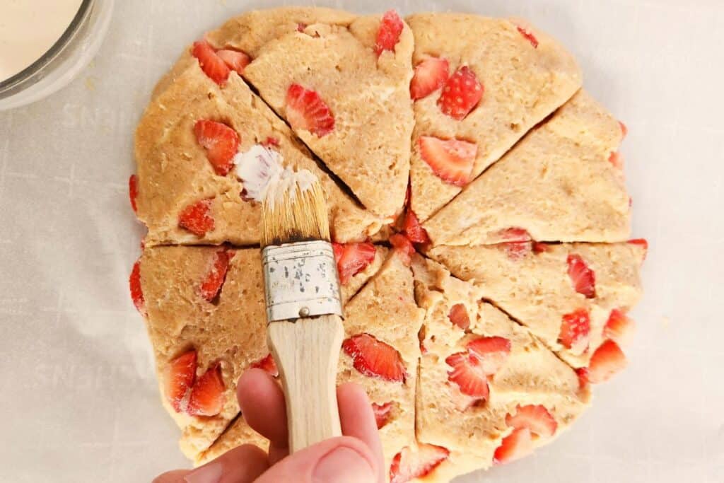 Using a pastry brush to brush heavy cream on strawberry scone dough before baking.