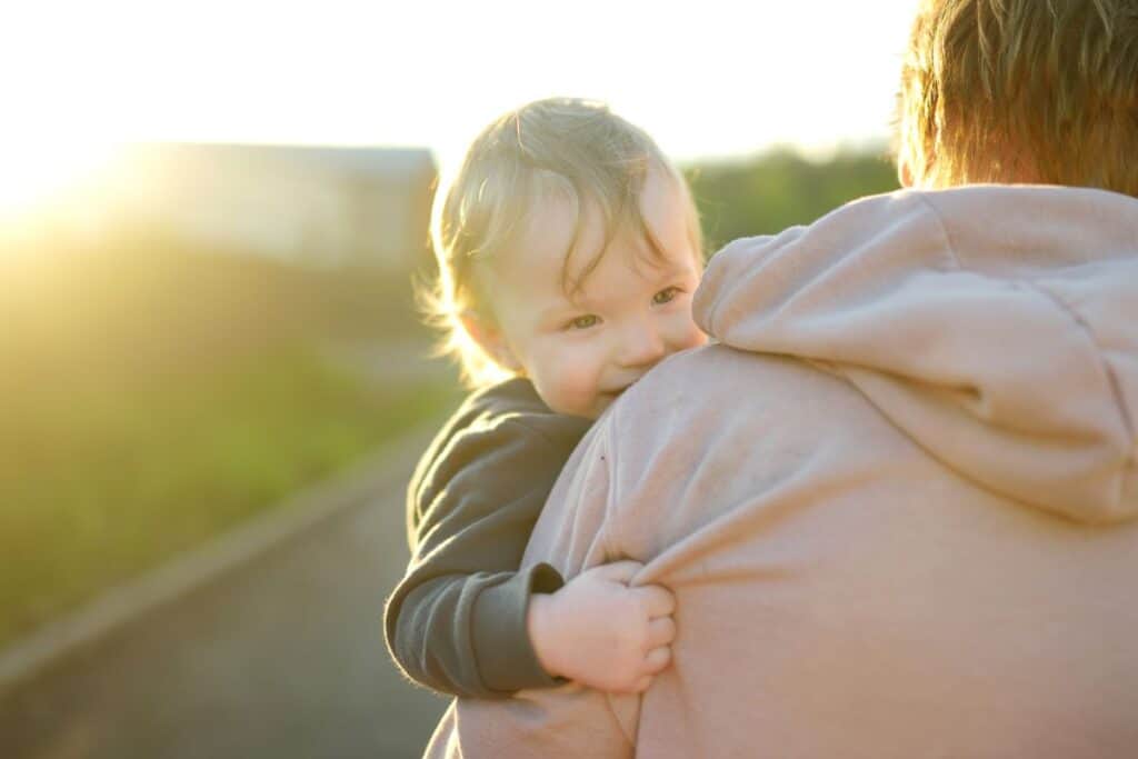 Clingy toddler held by mom, looking over her shoulder.