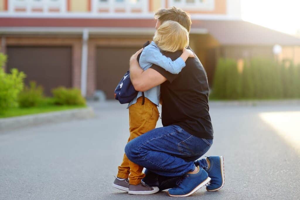Dad hugging preschool son in the driveway.