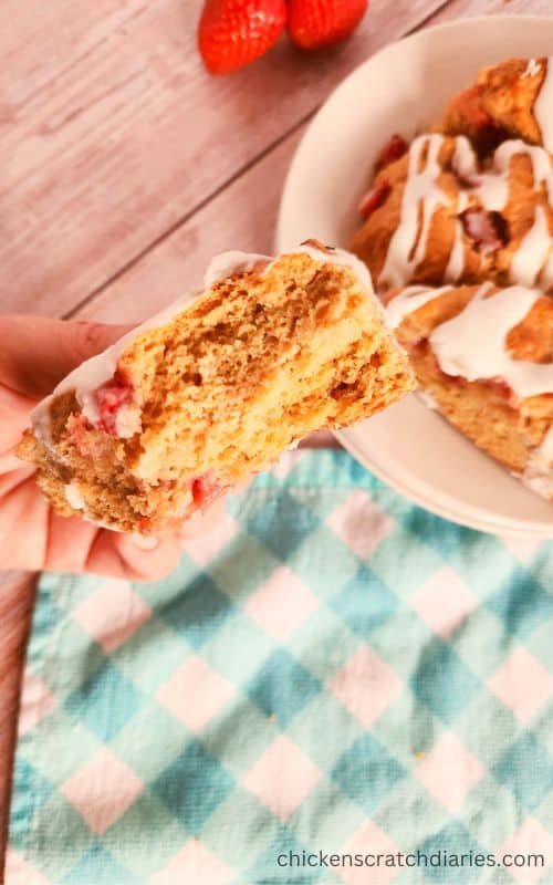 Holding a piece of strawberry scone above a plate with more glazed scones.