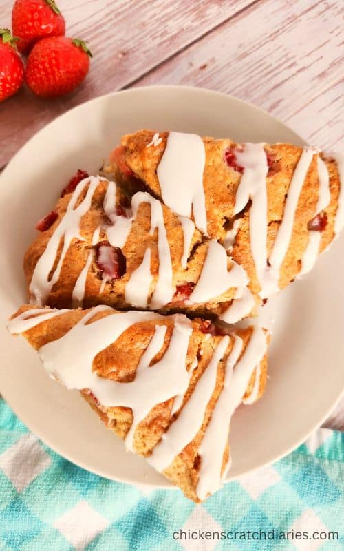 3 Glazed strawberry scones on a white plate on a teal and white checked tea towel.