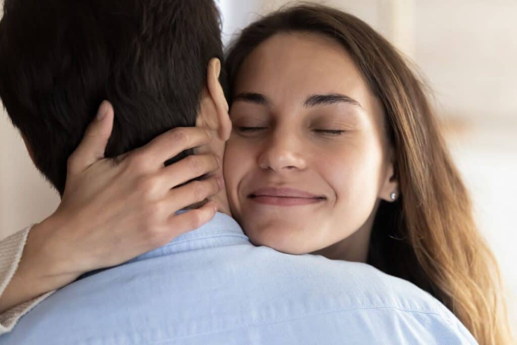 Closeup of woman hugging her husband with eyes closed, smiling.