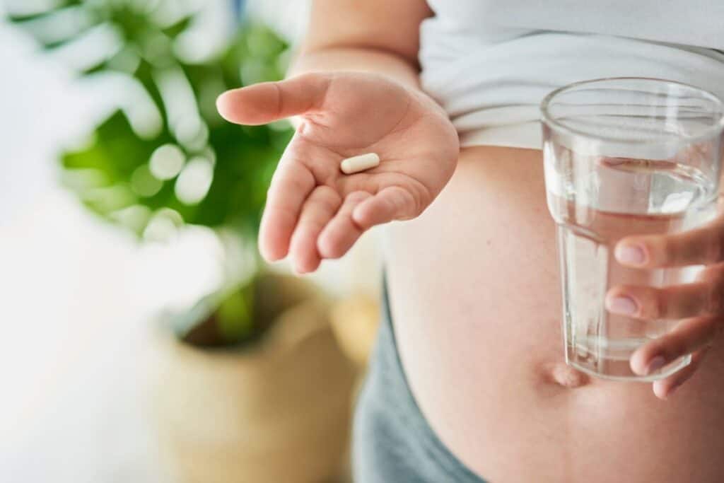 Pregnant woman holding a vitamin in her hand with a glass of water.