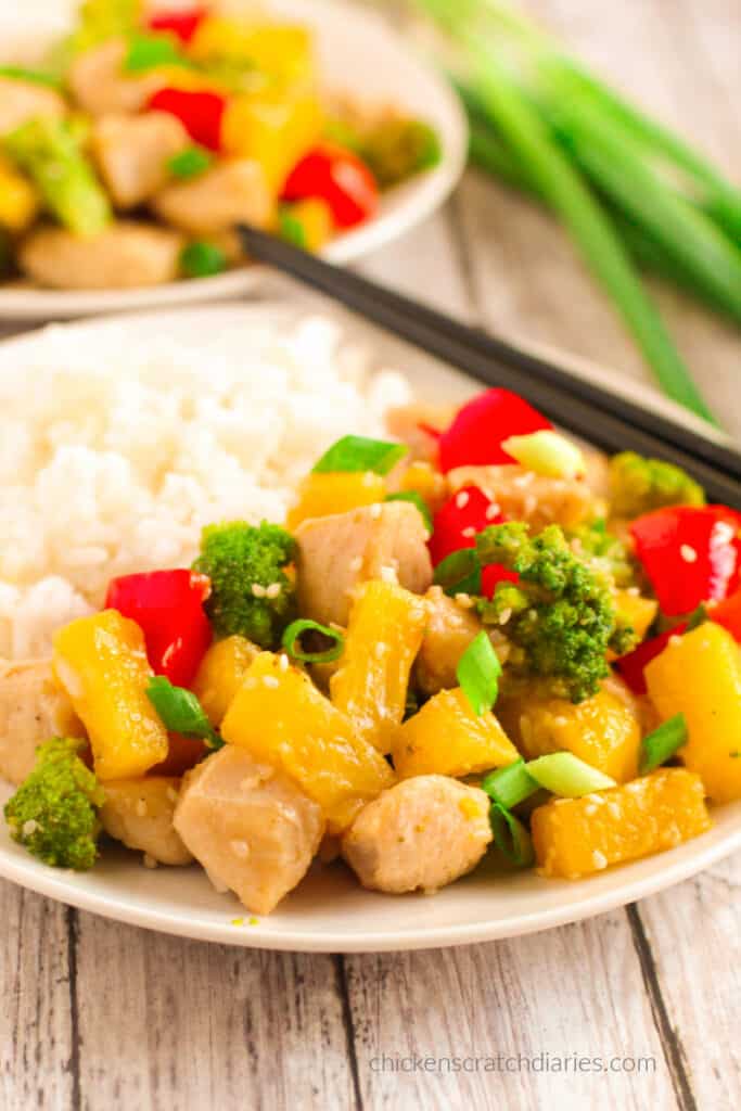 Two plates of pineapple chicken stir fry on a white wood table.