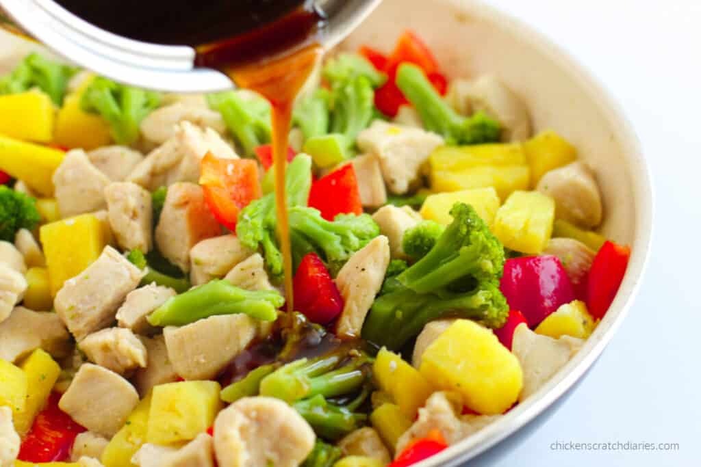 Pouring the sauce over the Hawaiian chicken pineapple stir-fry in a skillet.