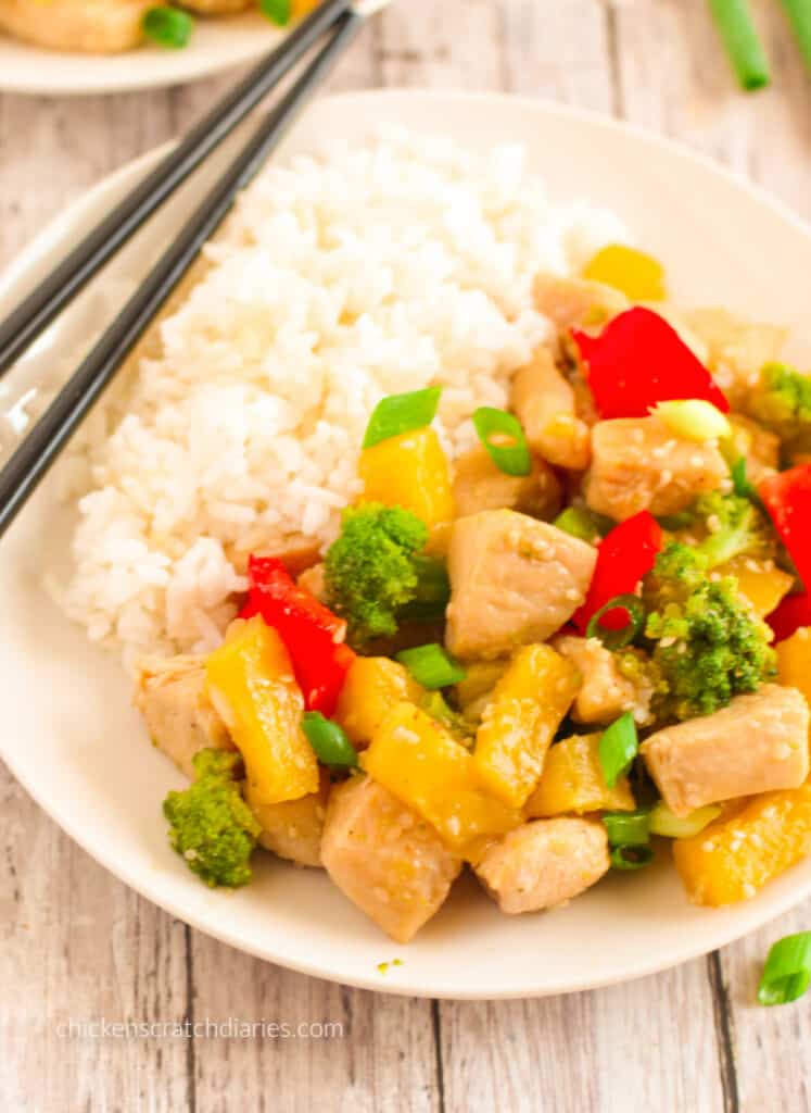 Pineapple chicken stir-fry with rice on a white plate with chopsticks .