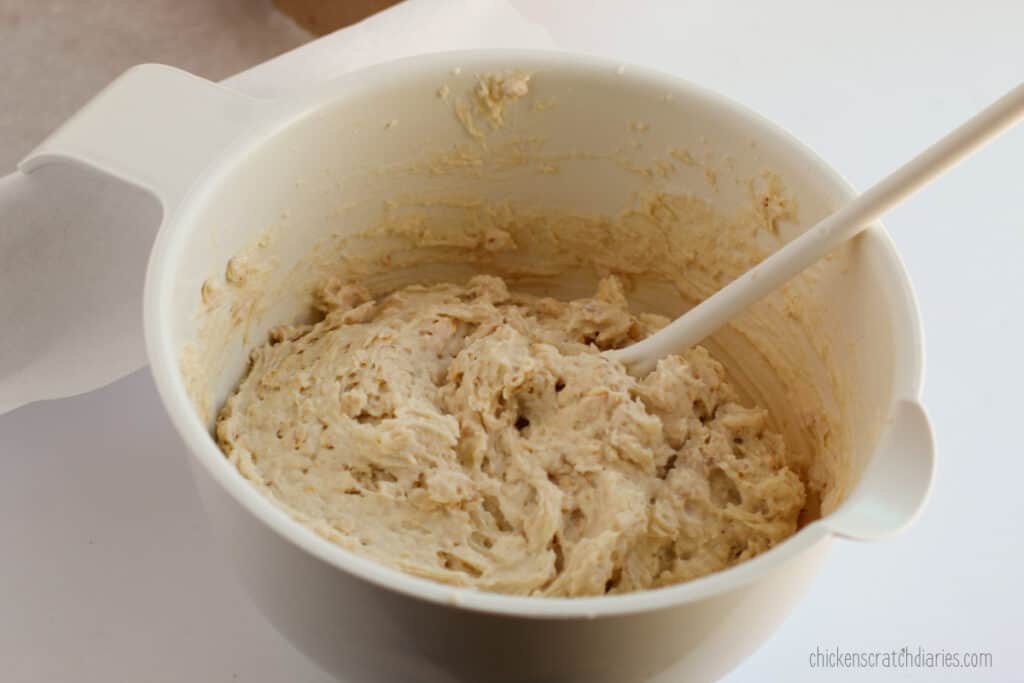 Oat bread batter in a white mixing bowl with a white mixing spoon.