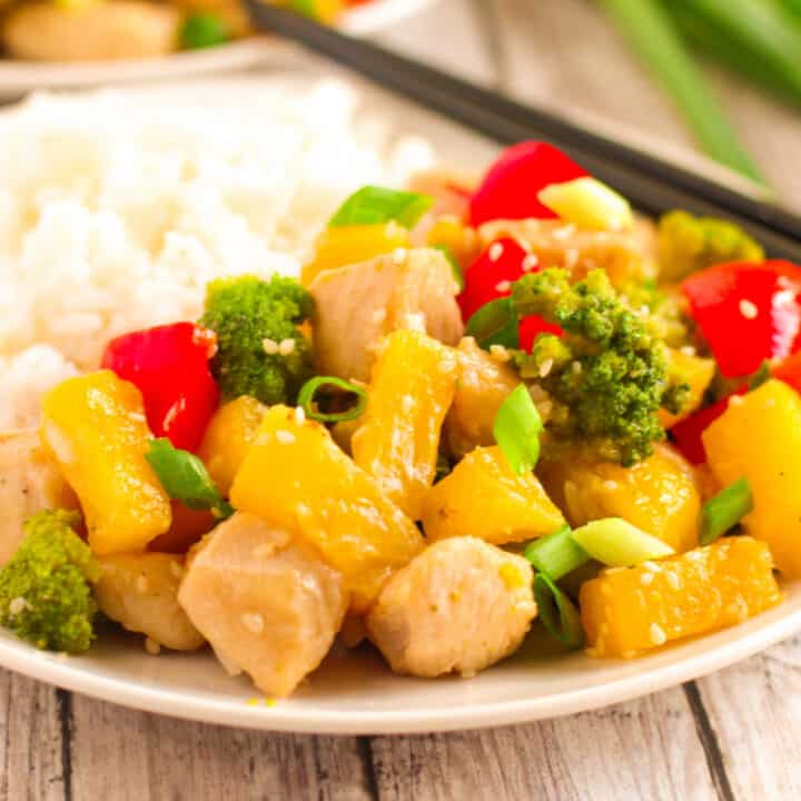 Hawaiian pineapple chicken stir fry with rice on a white plate with green onion in the background.