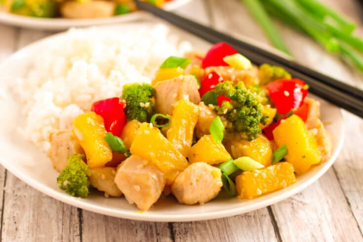 Hawaiian pineapple chicken stir fry with rice on a white plate with green onion in the background.