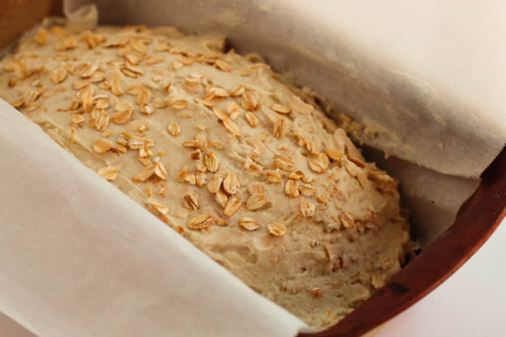 Quick oat bread in a loaf pan with parchment paper, ready to bake.