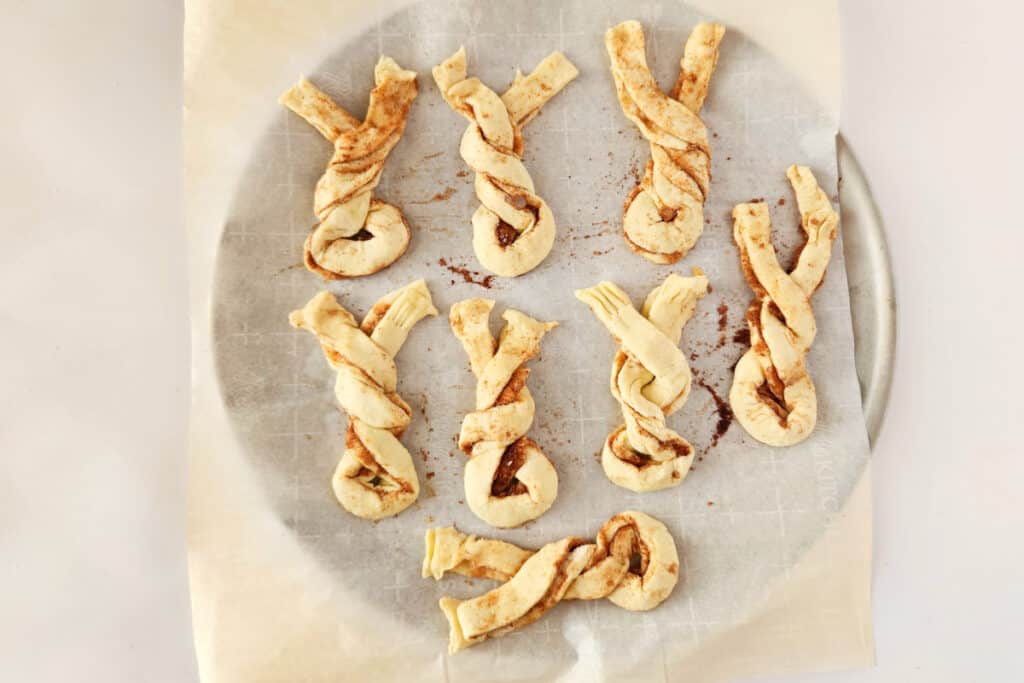 Making the cinnamon twist puff pastries by twisting them into Easter bunny ear shape, on a parchment paper.