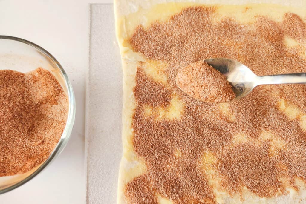 Process of sprinking the cinnamon sugar mixture over the puff pastry sheets.