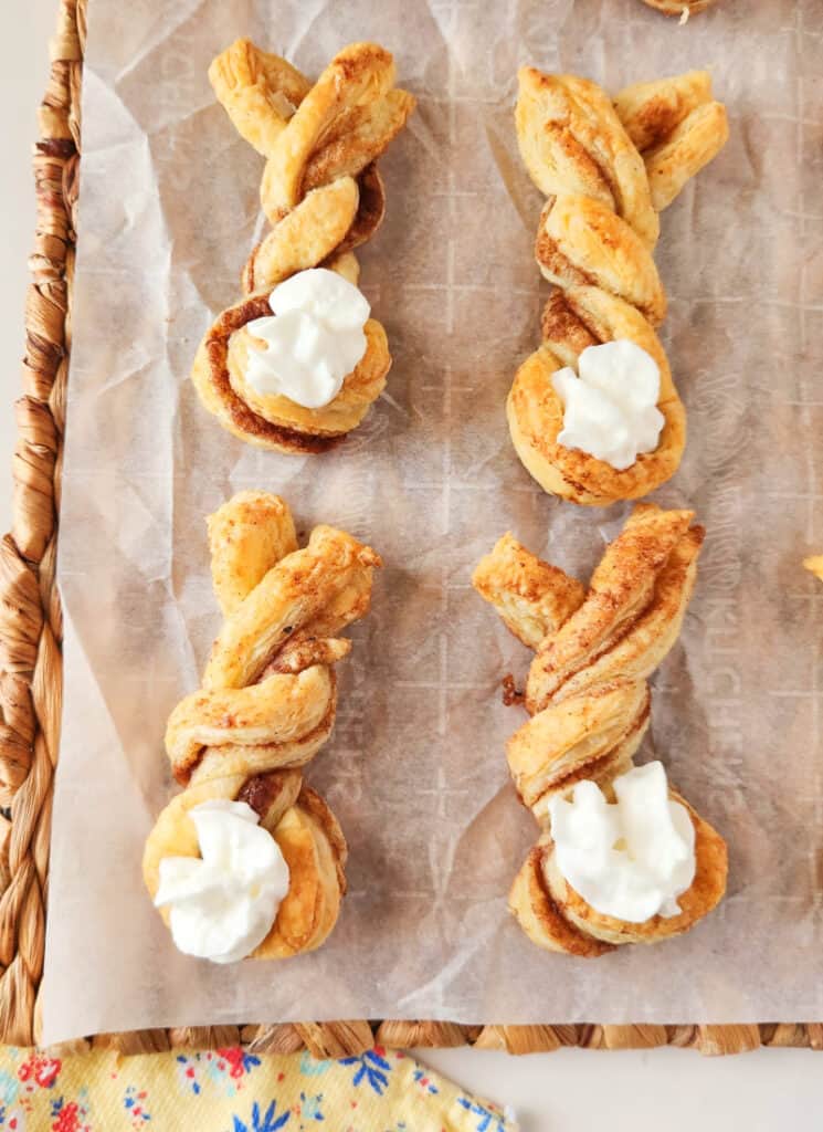 Baked cinnamon puff pastry twists on a parchment paper and woven placemat background.