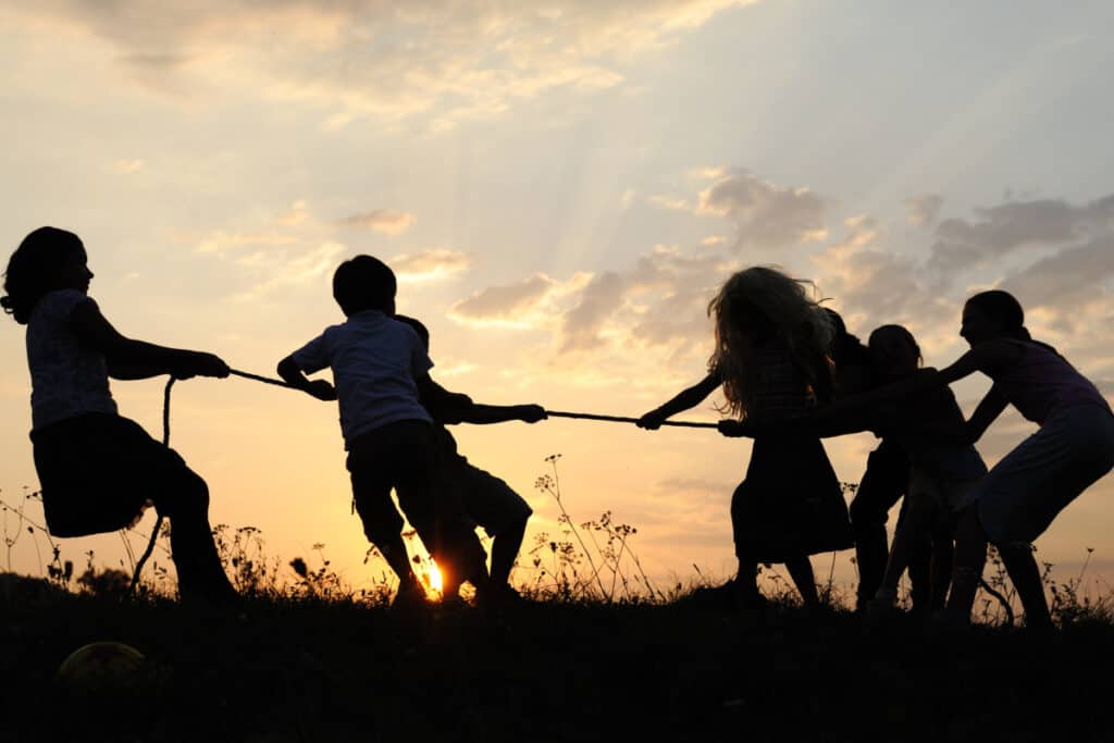 Family playing tug of war with sunset in background.