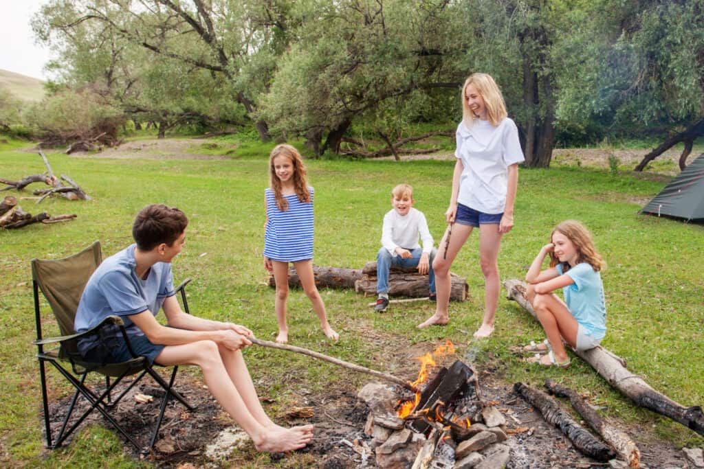 Mom and four kids building a fire and roasting food outside.