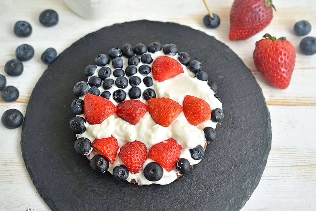 Close up of red, white and blue cookie pizza decorated with cream cheese and fresh strawberries and blueberries.