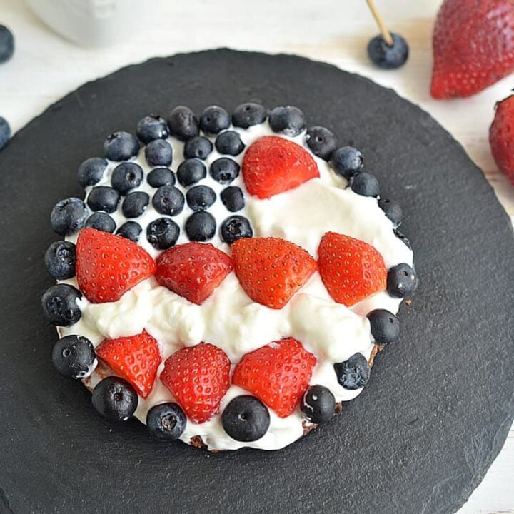 Finished cookie pizza with strawberries and blueberries on a pizza stone.