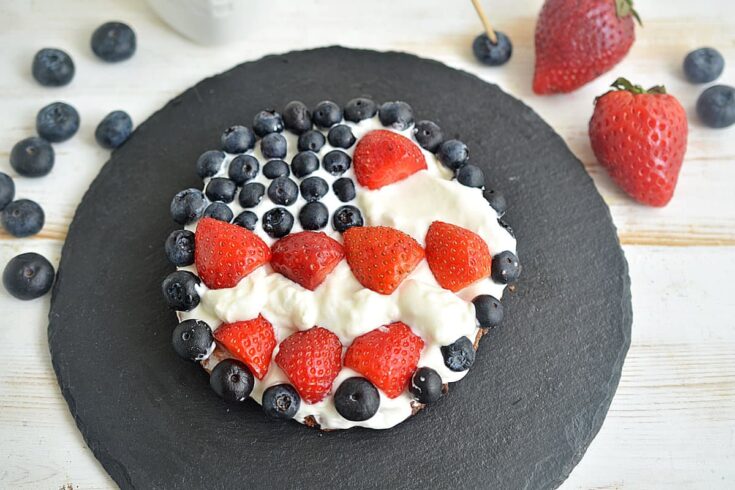 Finished cookie pizza with strawberries and blueberries on a pizza stone.