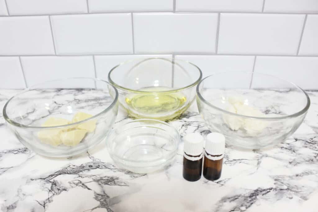 Body Butter ingredients in glass bowls: cocoa butter, avocado oil, shea butter, vitamin E oil and essential oils.