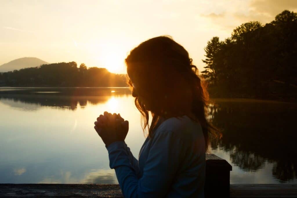 Woman praying at sunset with lake in background.