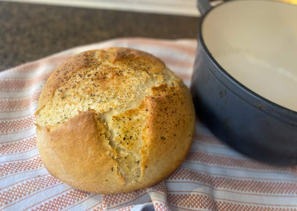 Crusty artisan bread loaf next to dutch oven, cooling on a tea towel.