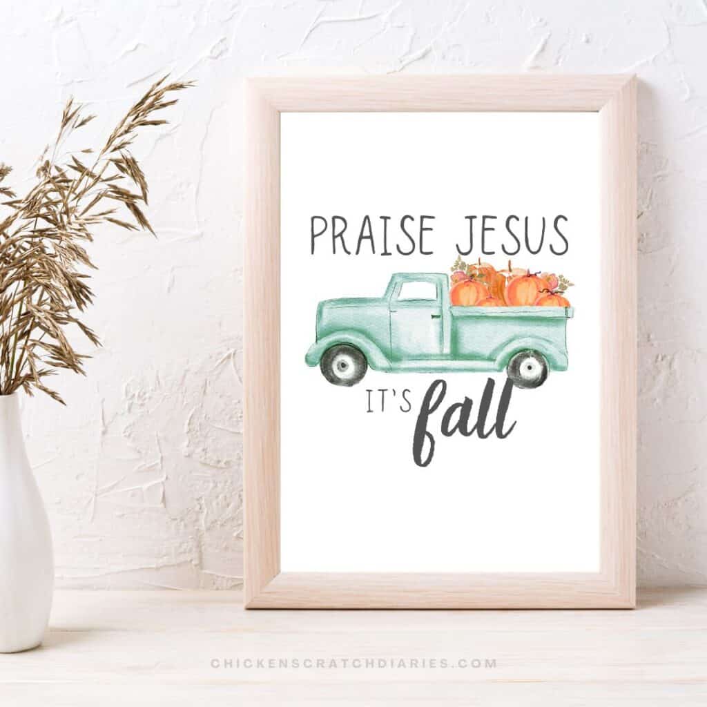 Printed artwork of watercolor teal pickup truck with pumpkins in the bed. Picture is framed and sitting on a wooden desk near a faux plant.