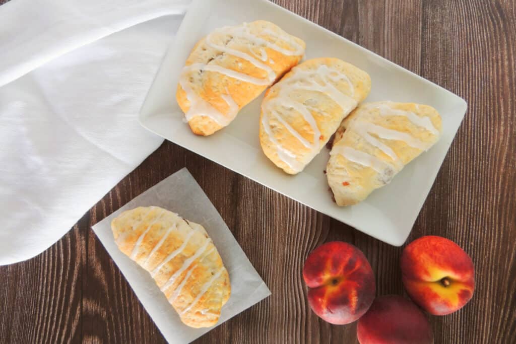 Peach pie turnovers on a plate with peaches on wooden table.