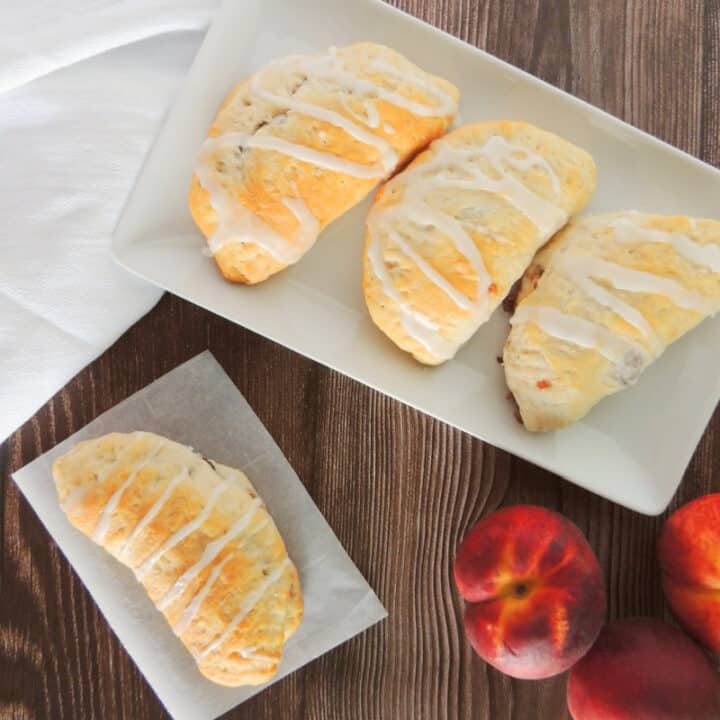 Peach pie turnovers on a plate with peaches on wooden table.