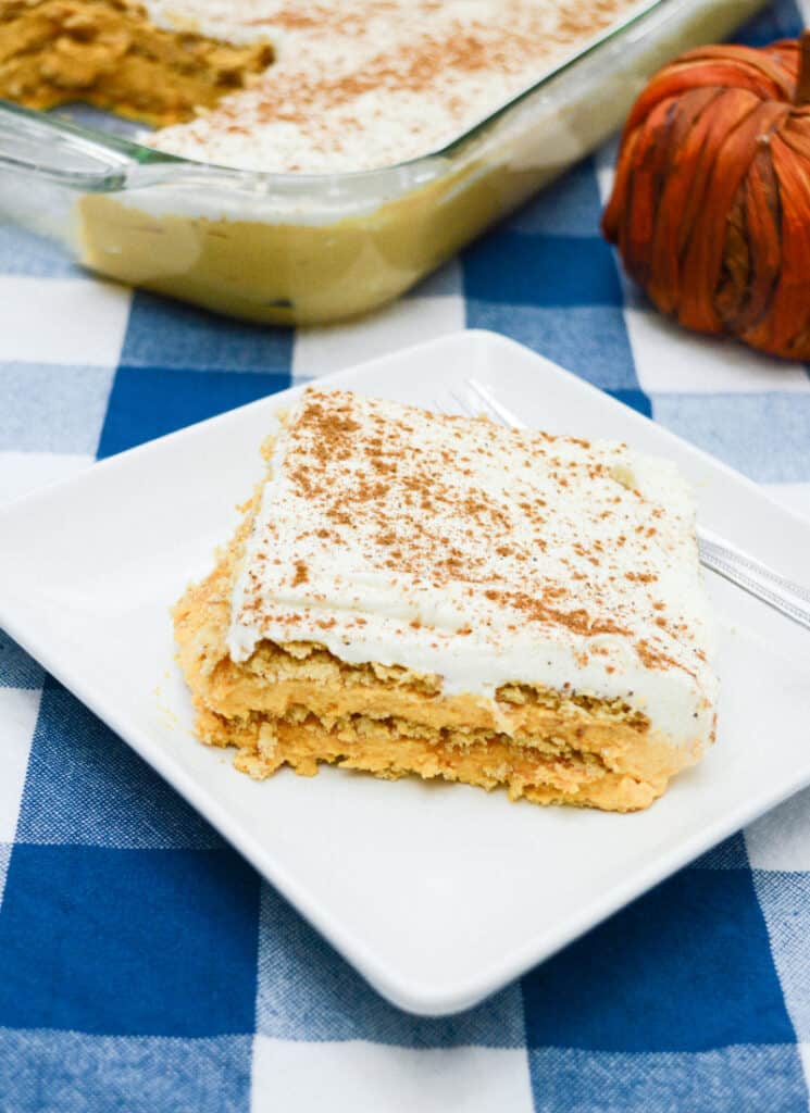 Slice of pumpkin icebox cake on a white square plate on blue checkered tablecloth with pumpkin decor.