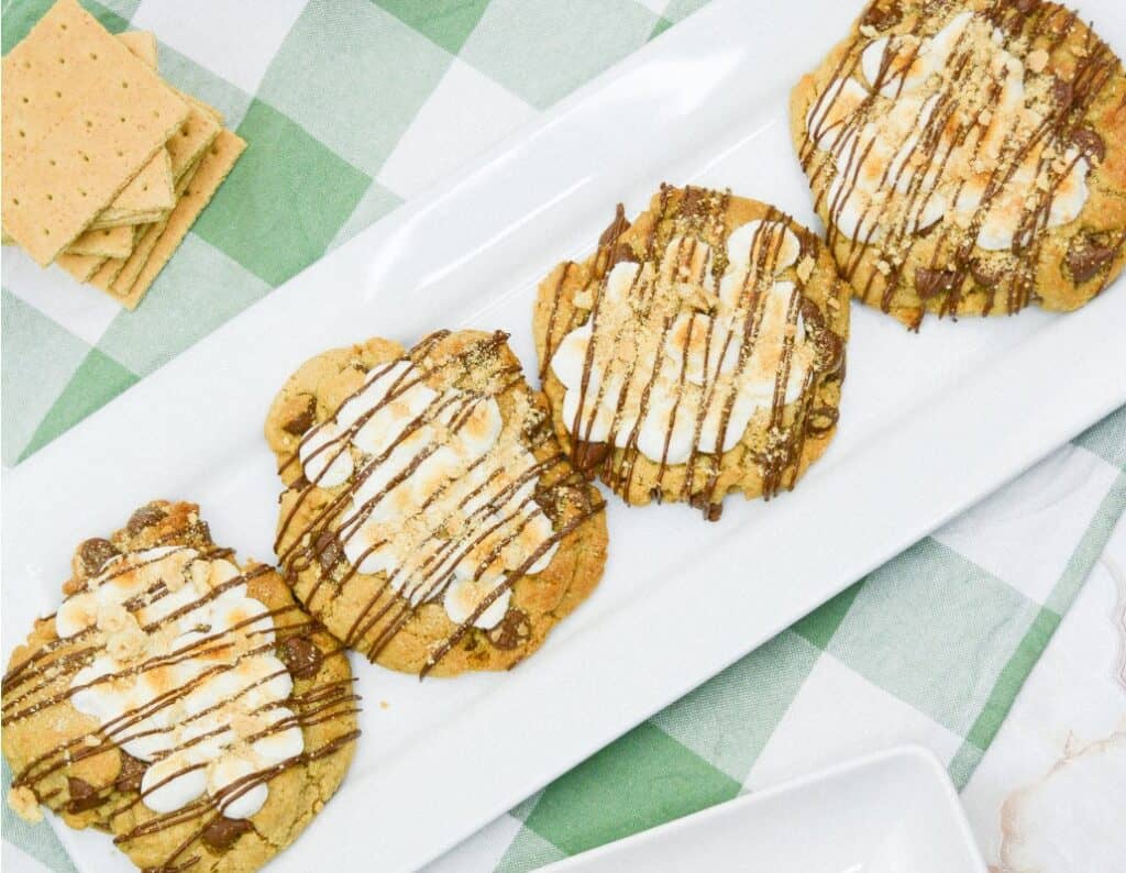 Four smores chocolate chip cookies in a row on a long white platter.