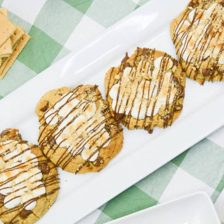 Four smores chocolate chip cookies in a row on a long white platter.
