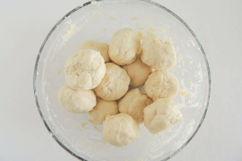 Biscuit dough balls in a clear glass bowl.
