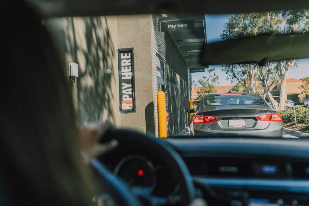 Woman in car, going through drive-thru lane of fast food restaurant.