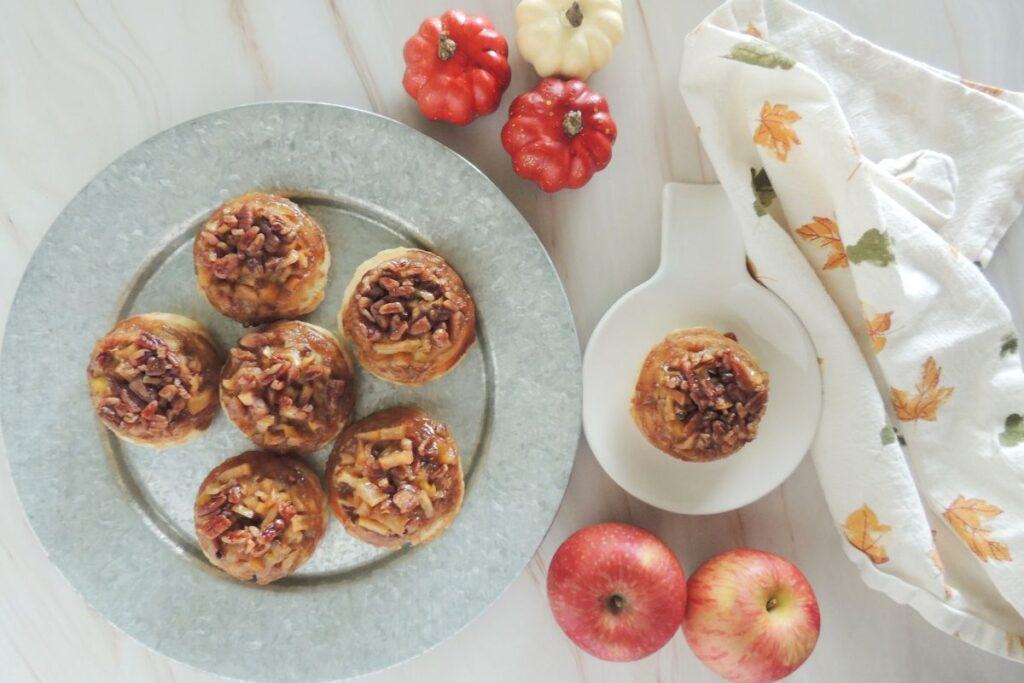 Caramel apple biscuits on a tin plate with apples and pumpkin decor nearby.