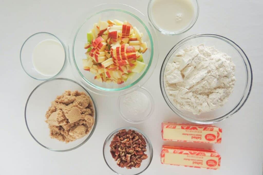 Apple caramel biscuit ingredients in clear bowls on a white background.