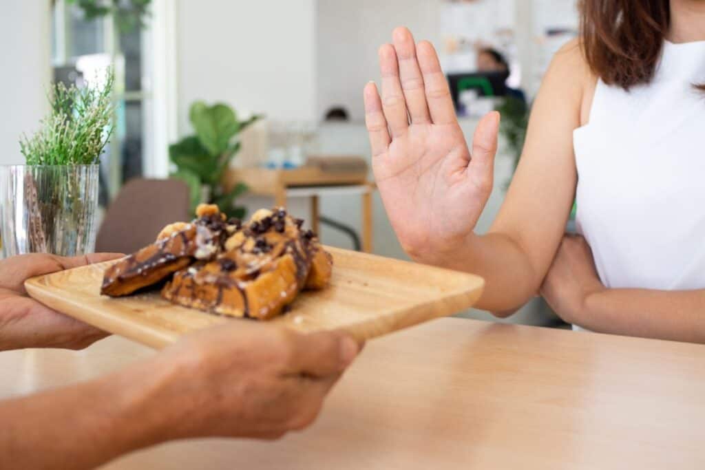 Woman holding up hand for saying "no" to baked sweets.