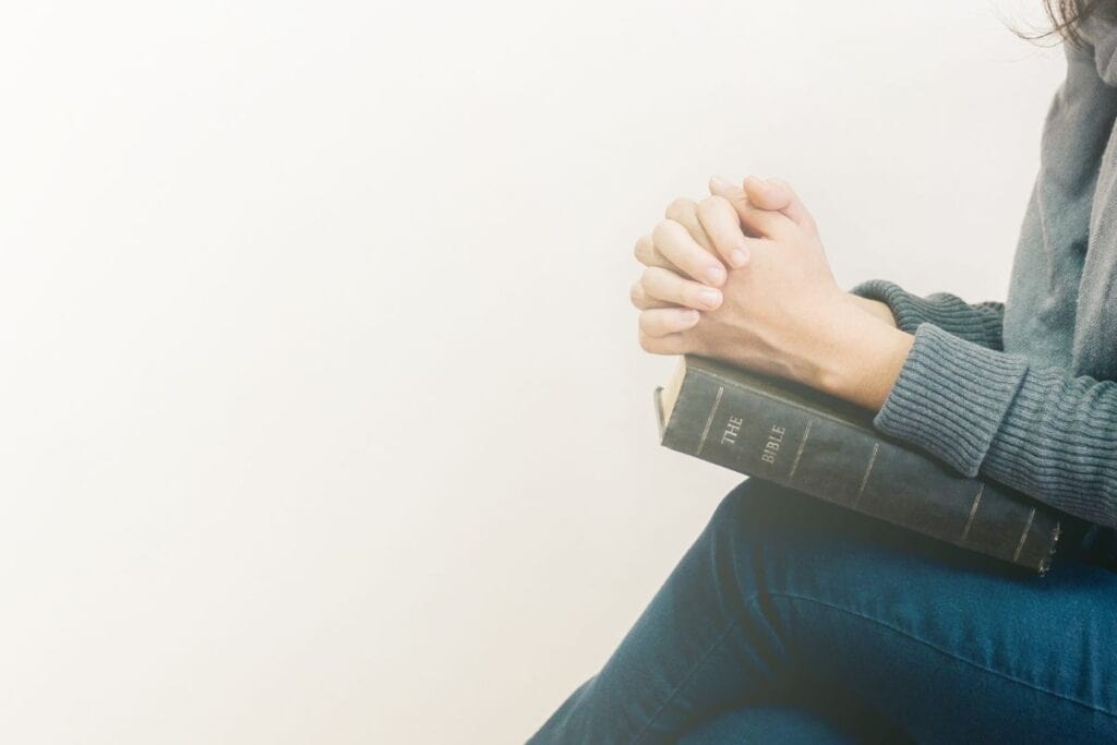 Woman with hands folded over her Bible in prayer.