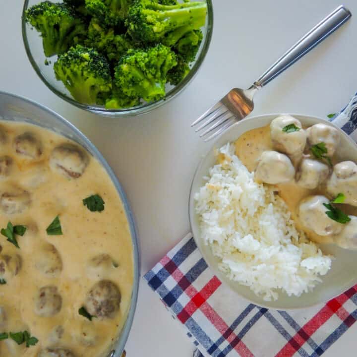 Swedish meatballs on plate with rice and brocolli on the side and skillet with meatballs on table.