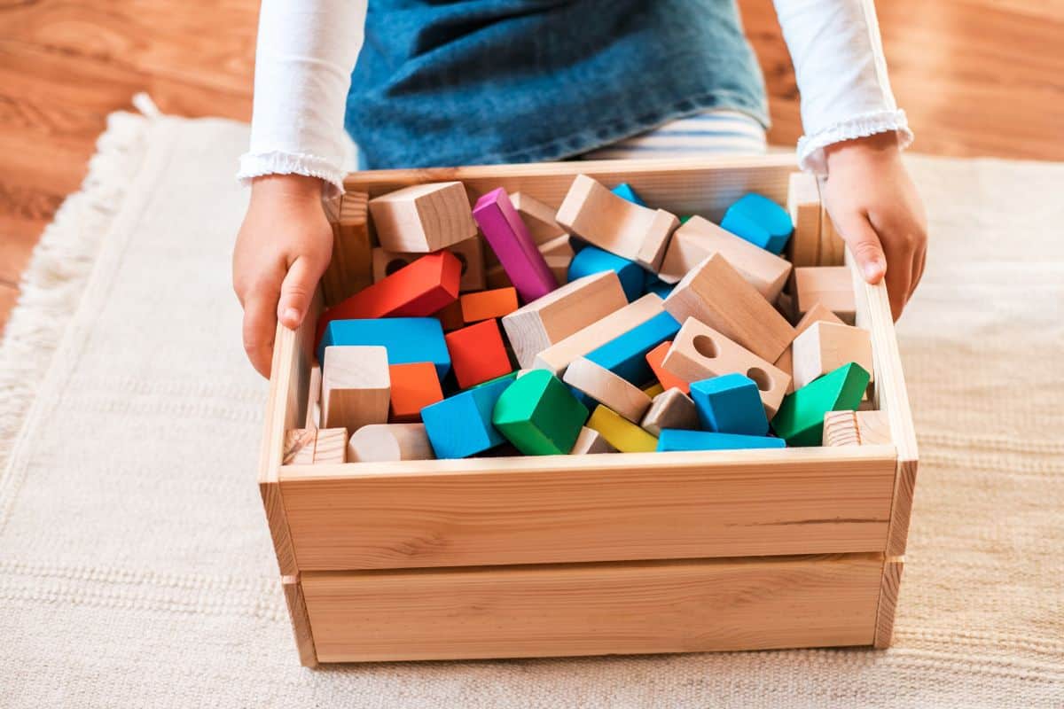 Little girl holding a wooden bin of blocks.