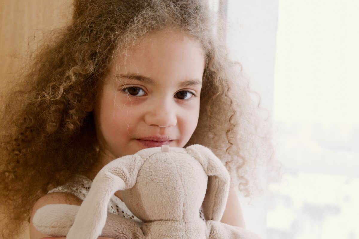 Little girl holding stuffed rabbit in her room.