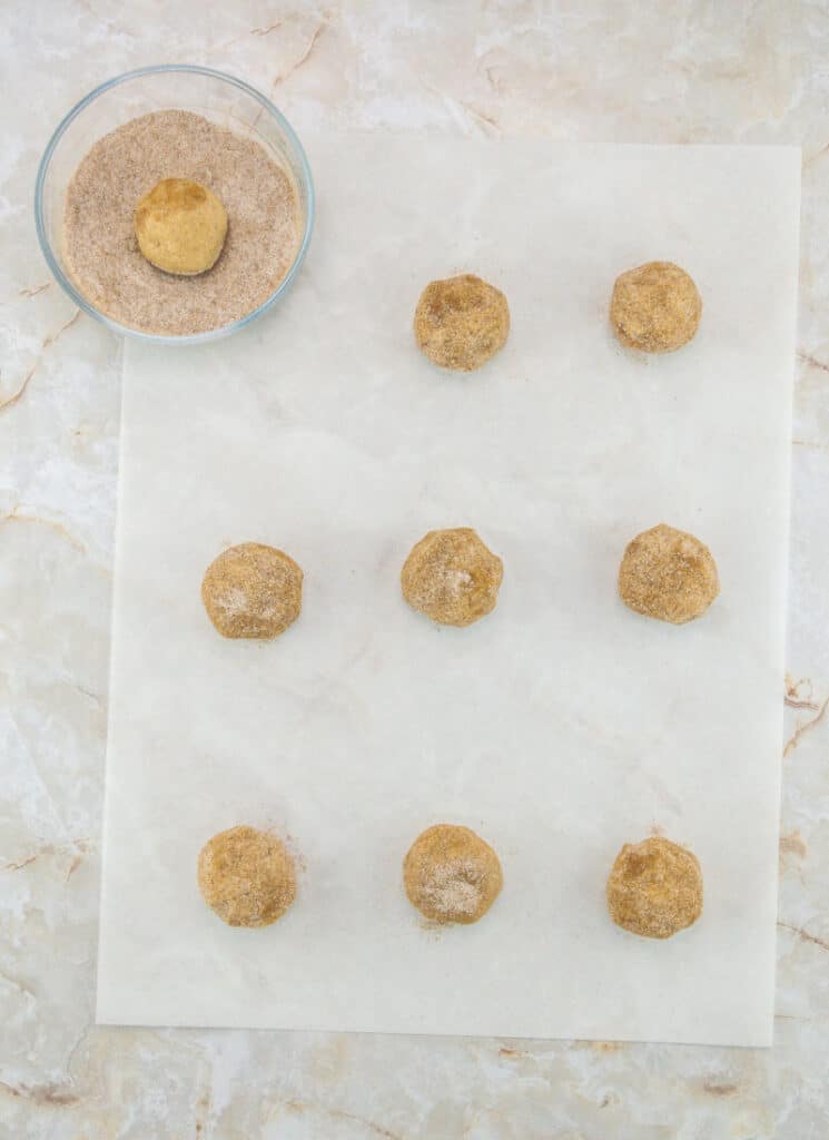 Dough balls spaced apart on parchment paper and rolled in chai spice mixture.