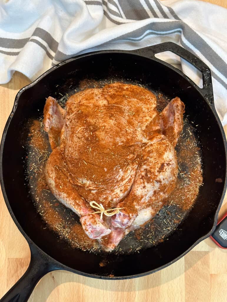 raw whole chicken coated with seasonings in a cast iron skillet, just before roasting.
