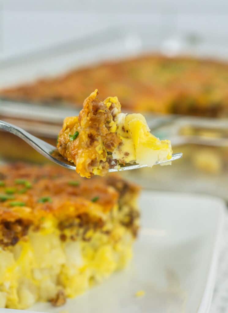 Closeup of forkful of hashbrown breakfast casserole with casserole in background.