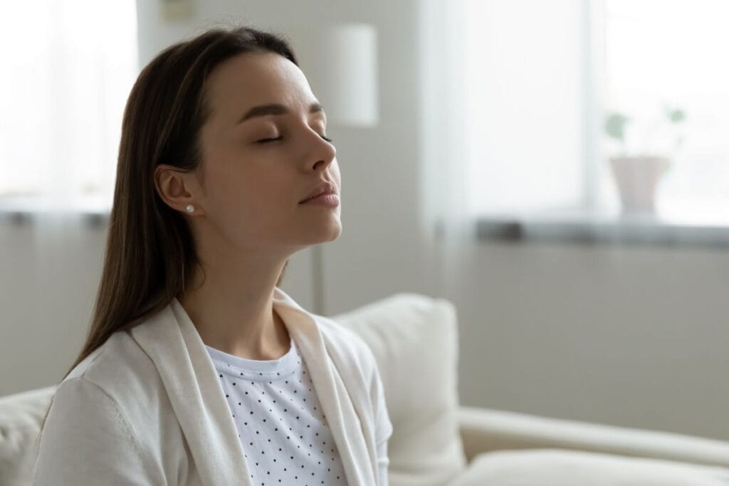 Young mom sitting on couch with eyes closed, praying.