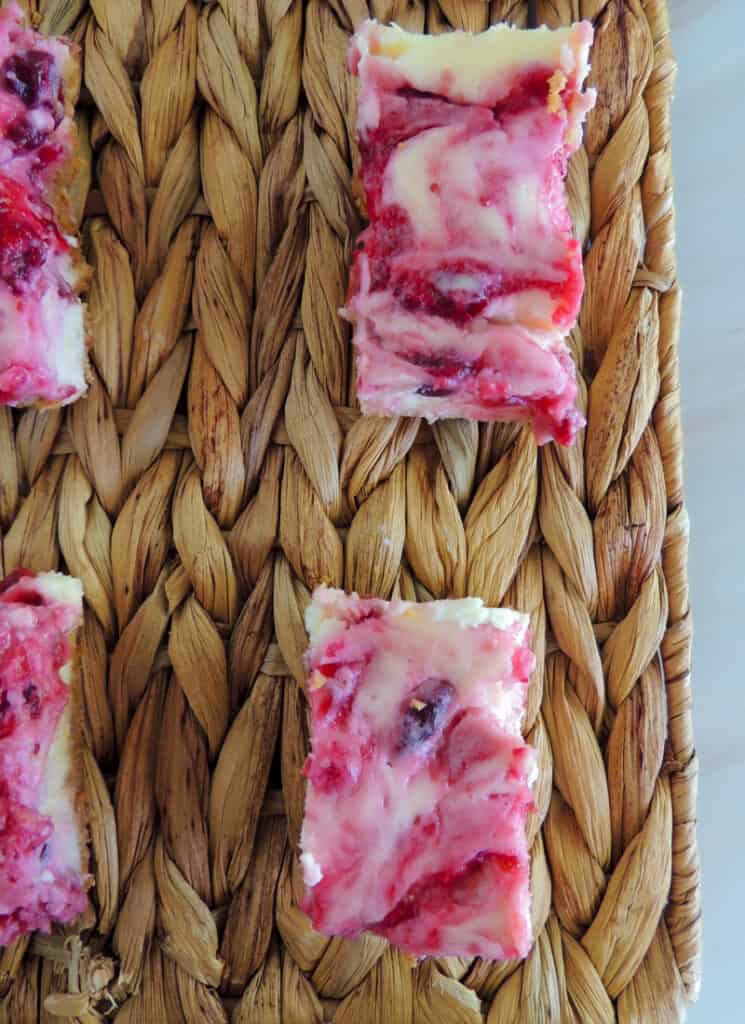 Closeup of cranberry lemon cheesecake bars on woven serving mat.