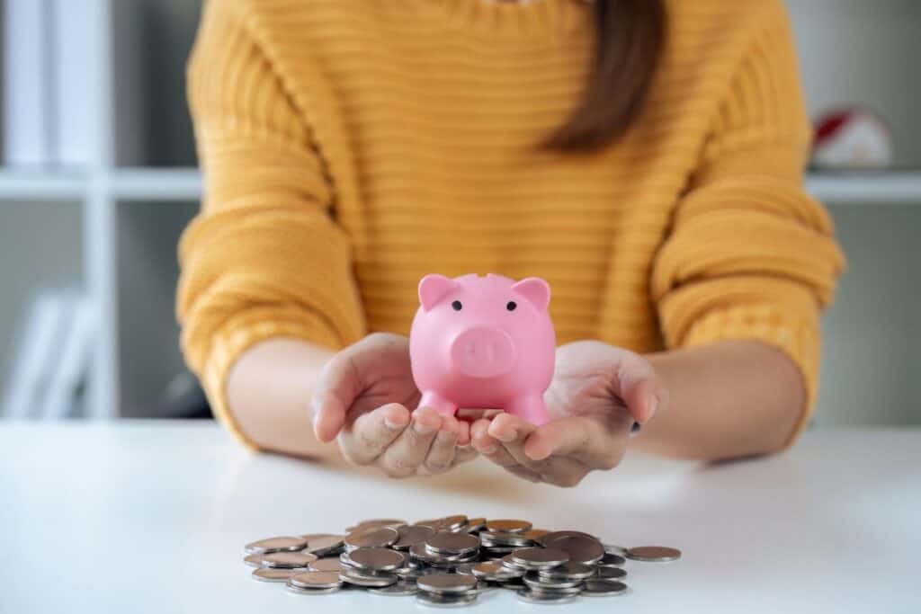 Woman in yellow sweater holding piggy bank with coins spilled on table. Saving money concept.